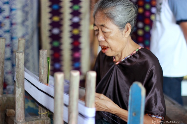 An old women is carefully starting a peace of woven fabric using traditional tools 